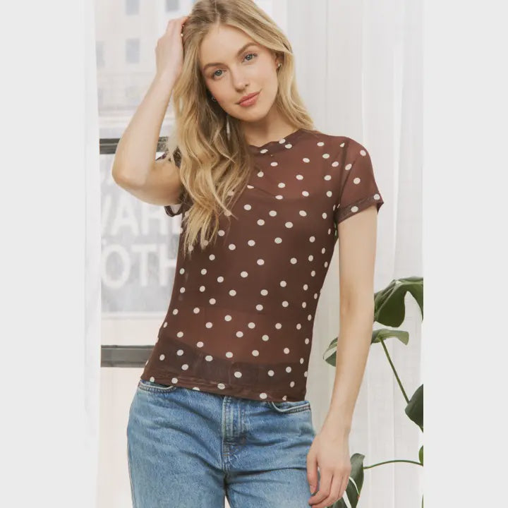 Woman wearing a brown polka dot shirt and blue jeans indoors.