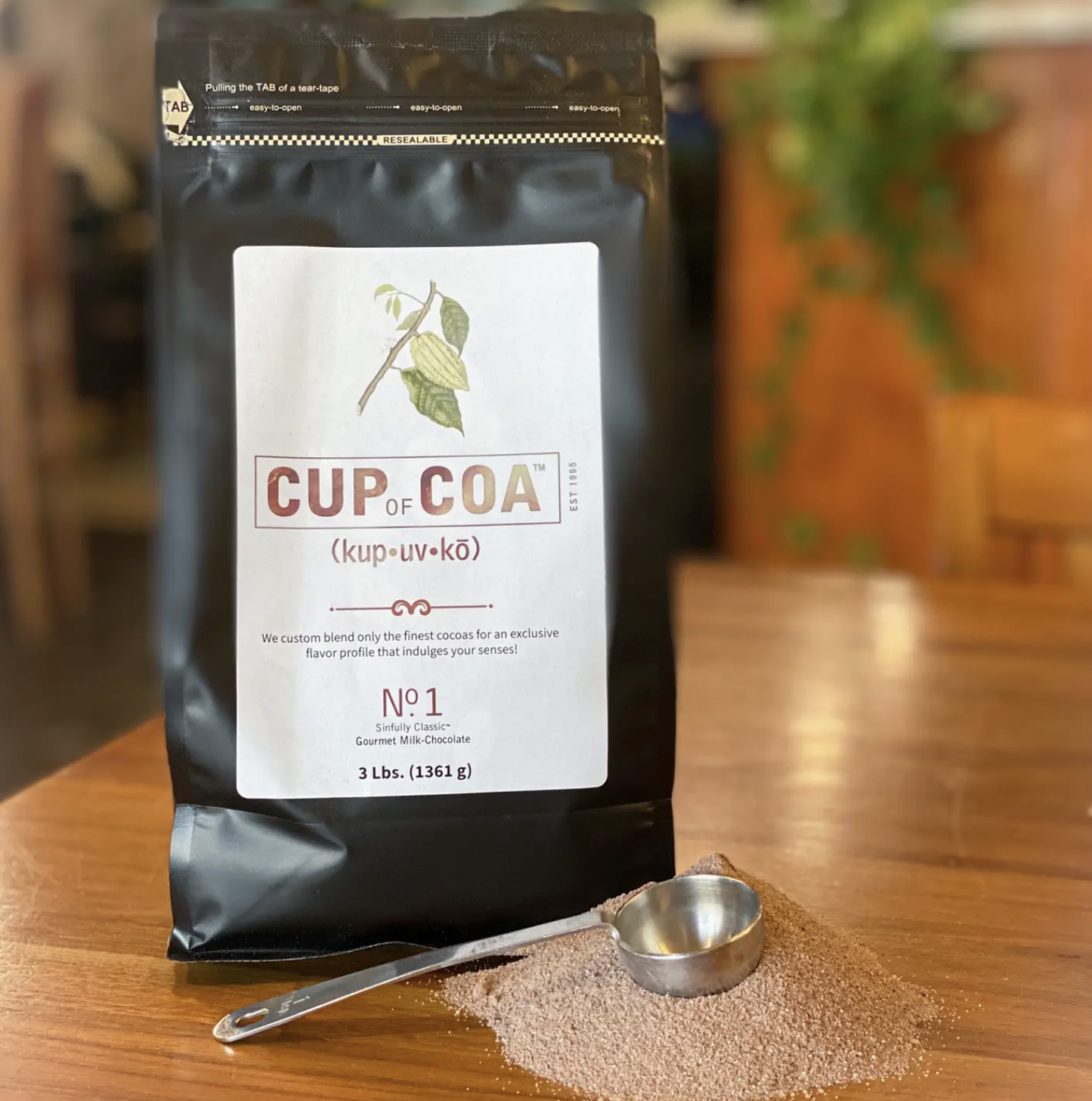 Cup of Coa coffee package on a wooden table with a spoonful of coffee grounds.
