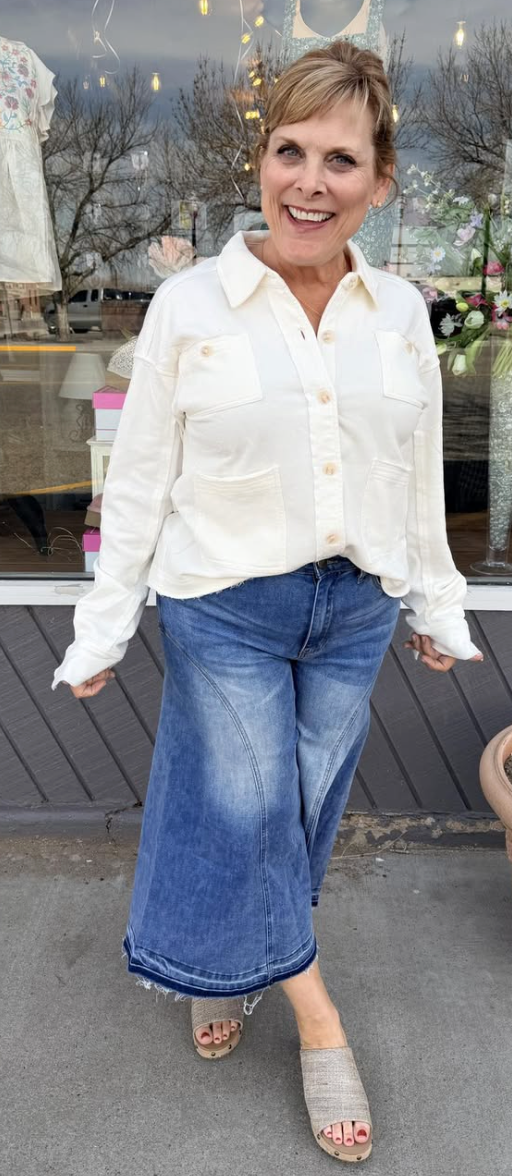 Woman wearing a white blouse and blue jeans standing outside a store.