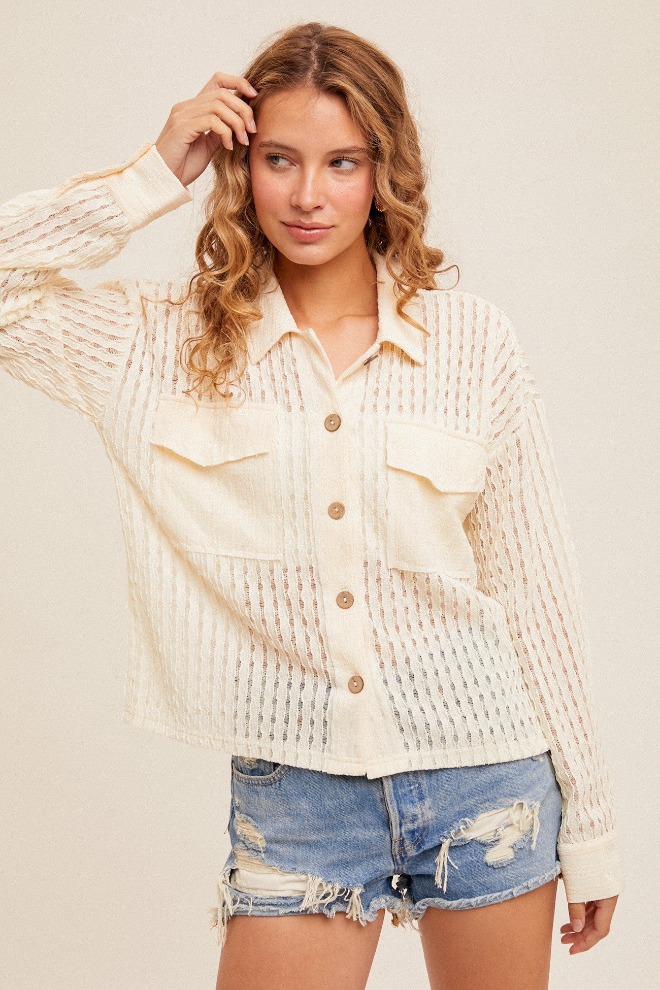 Woman wearing a textured beige jacket and denim shorts on a plain background