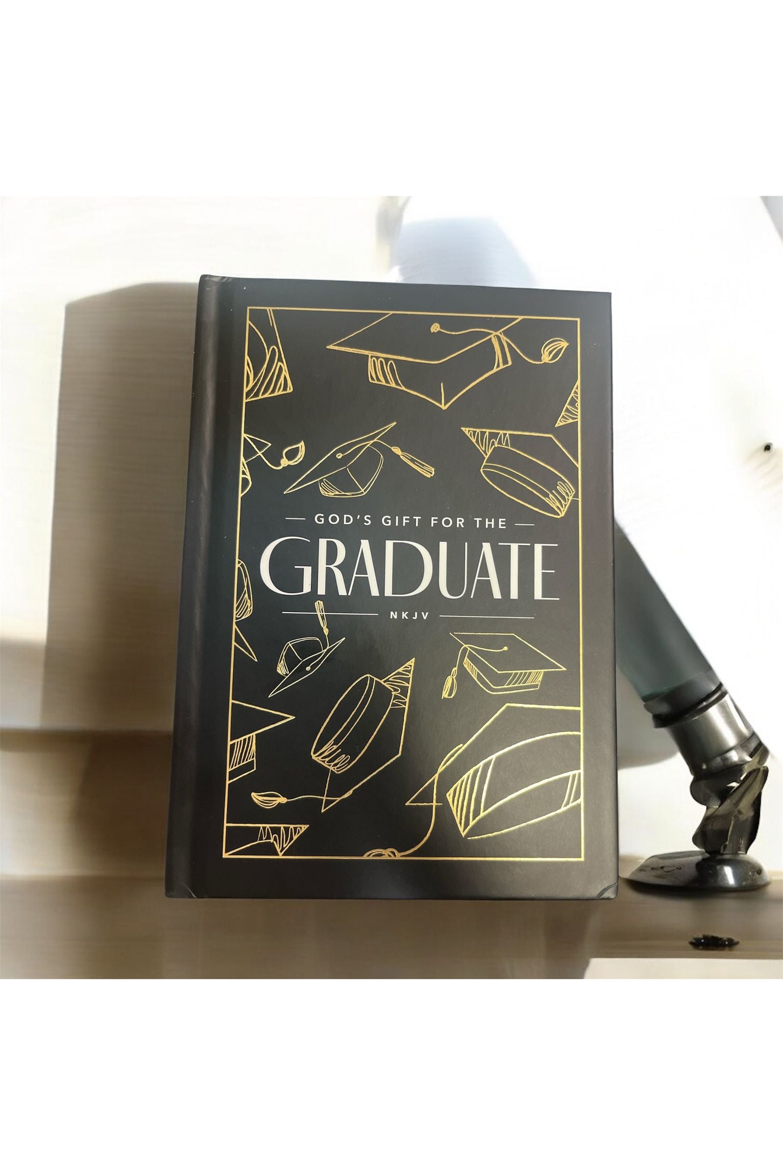 Book titled 'God's Gift for the Graduate' with gold illustrations on a wooden surface.