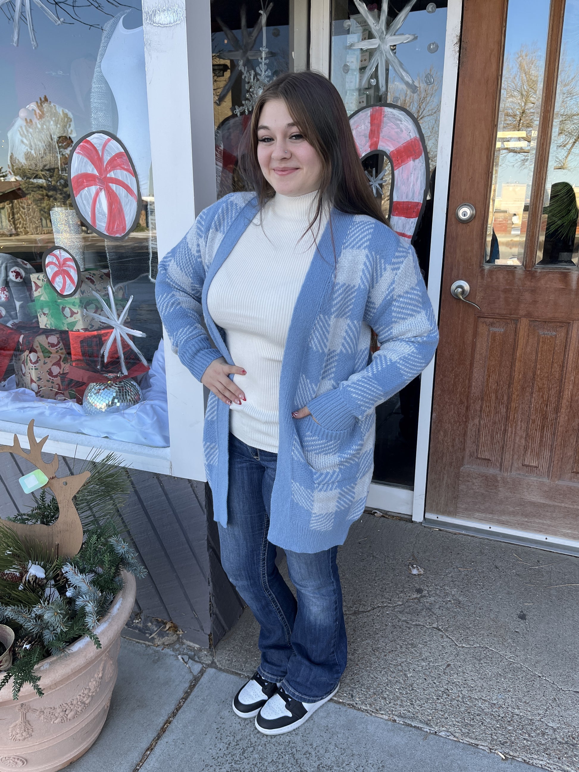 Woman wearing a blue patterned cardigan in front of a store with holiday decorations.