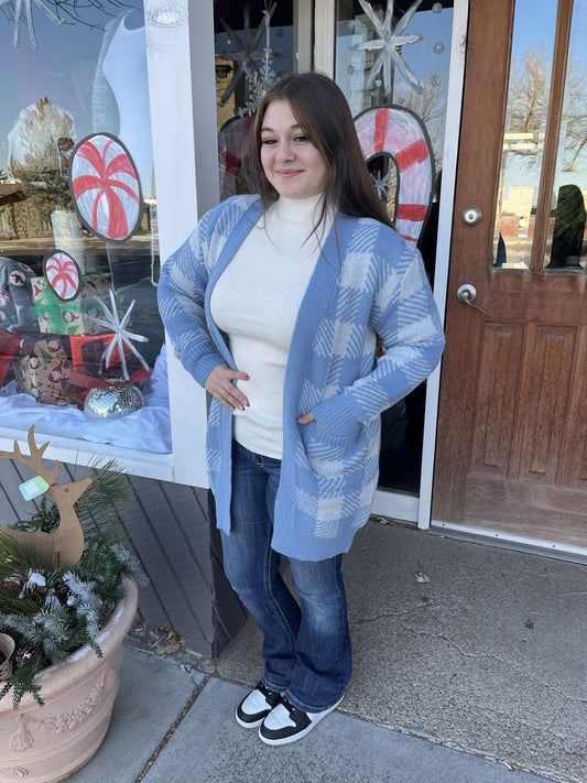 Woman wearing a blue patterned cardigan in front of a store with holiday decorations.