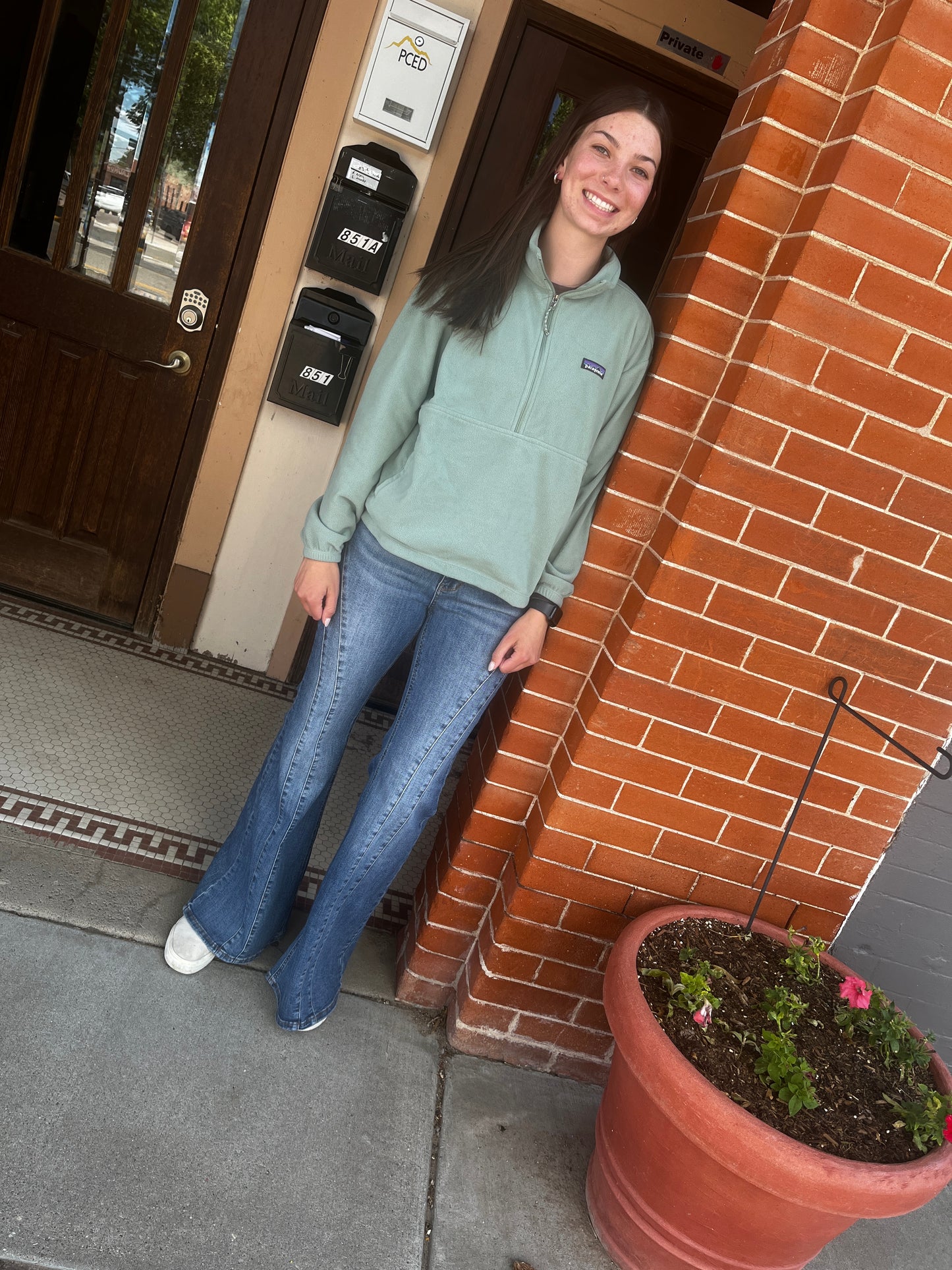 Person standing on a sidewalk next to a door with a plant pot nearby