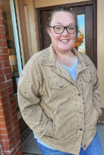 Person wearing a beige jacket standing in front of a door with a brick wall background