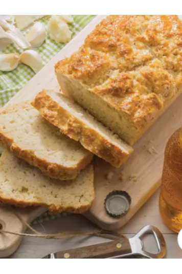 Loaf of bread with slices on a wooden cutting board, surrounded by beer bottles and a bottle cap.