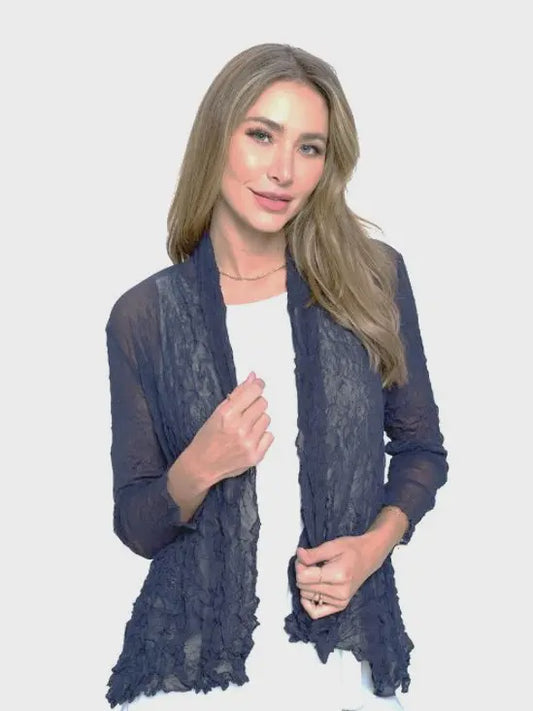 Woman wearing a navy blue lace cardigan over a white top on a light gray background