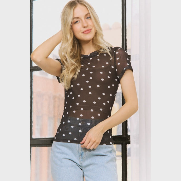Woman wearing a brown polka dot top and light blue jeans indoors.