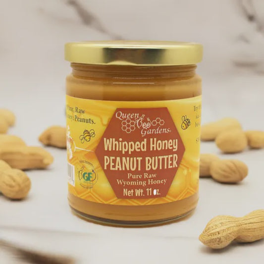 Jar of Queen Bee Gardens Whipped Honey Peanut Butter with peanuts around on a light background
