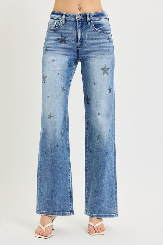 A person wearing light blue wide-leg denim jeans with scattered dark star patches, shown from the waist down against a plain light gray studio background.