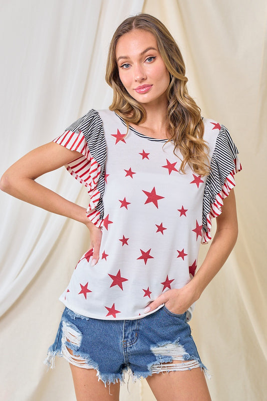 Woman wearing a white t-shirt with red star patterns and denim shorts against a beige curtain background