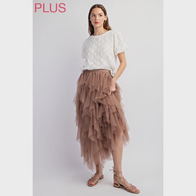 Woman wearing a white lace top and brown tiered skirt on a light gray background
