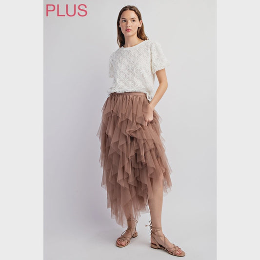Woman wearing a white lace top and brown tiered skirt on a light gray background