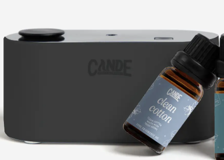 Black electronic device with 'Cande' branding and a bottle of 'Clean Cotton' oil on a white background.