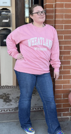 Person wearing a pink sweatshirt with 'Wheatland Wyoming' text, standing against a brick wall.