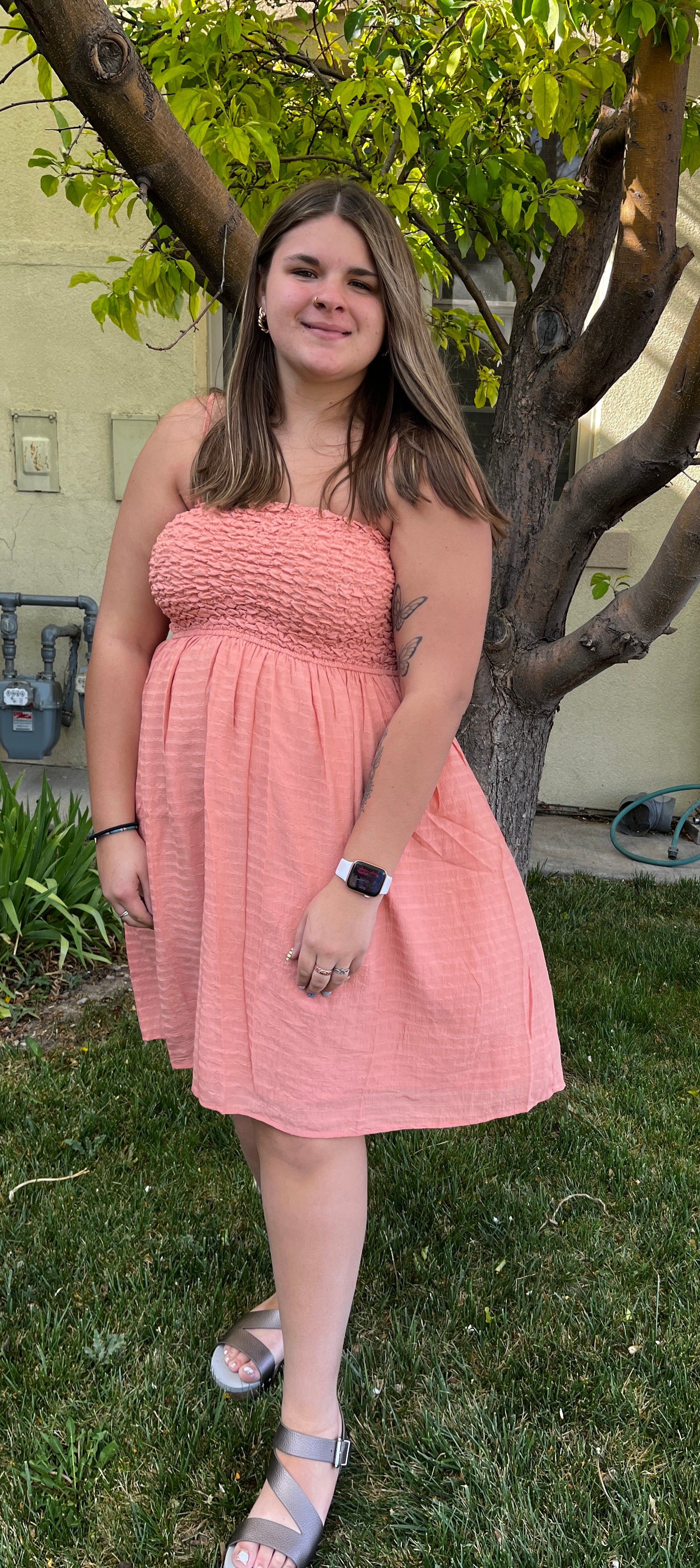 Woman in a pink dress standing outdoors near a tree
